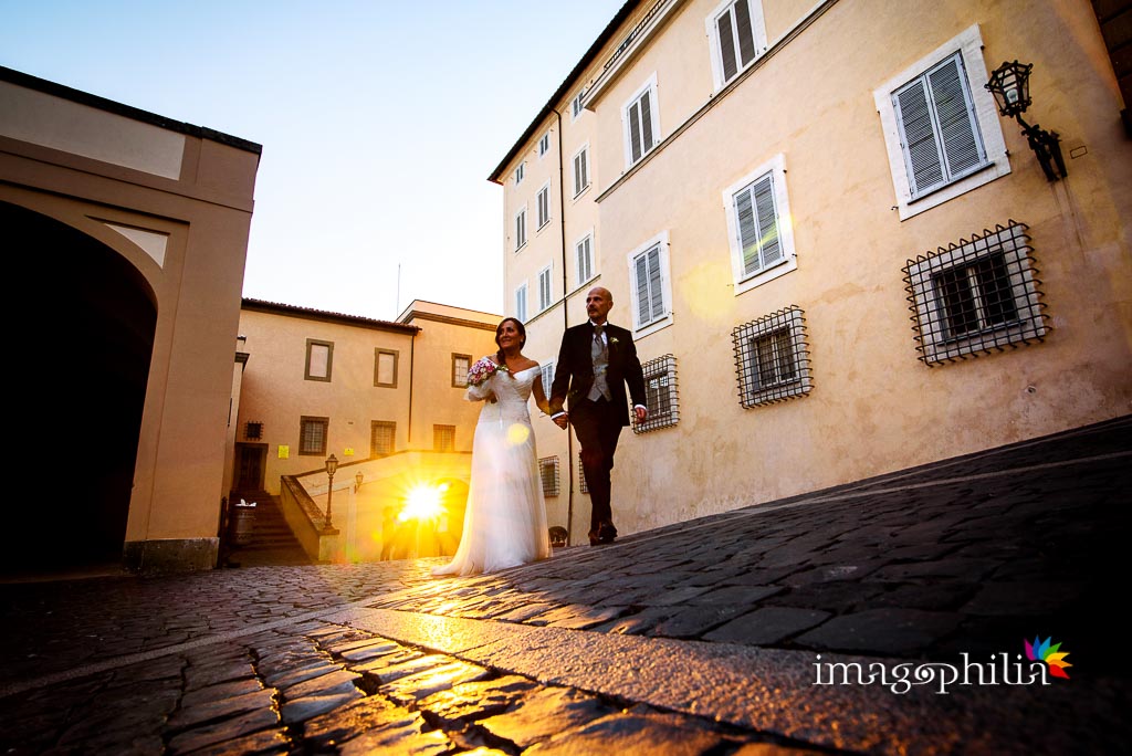Gli sposi entrano a Castel Gandolfo con la luce del tramonto che filtra dalla porta del borgo